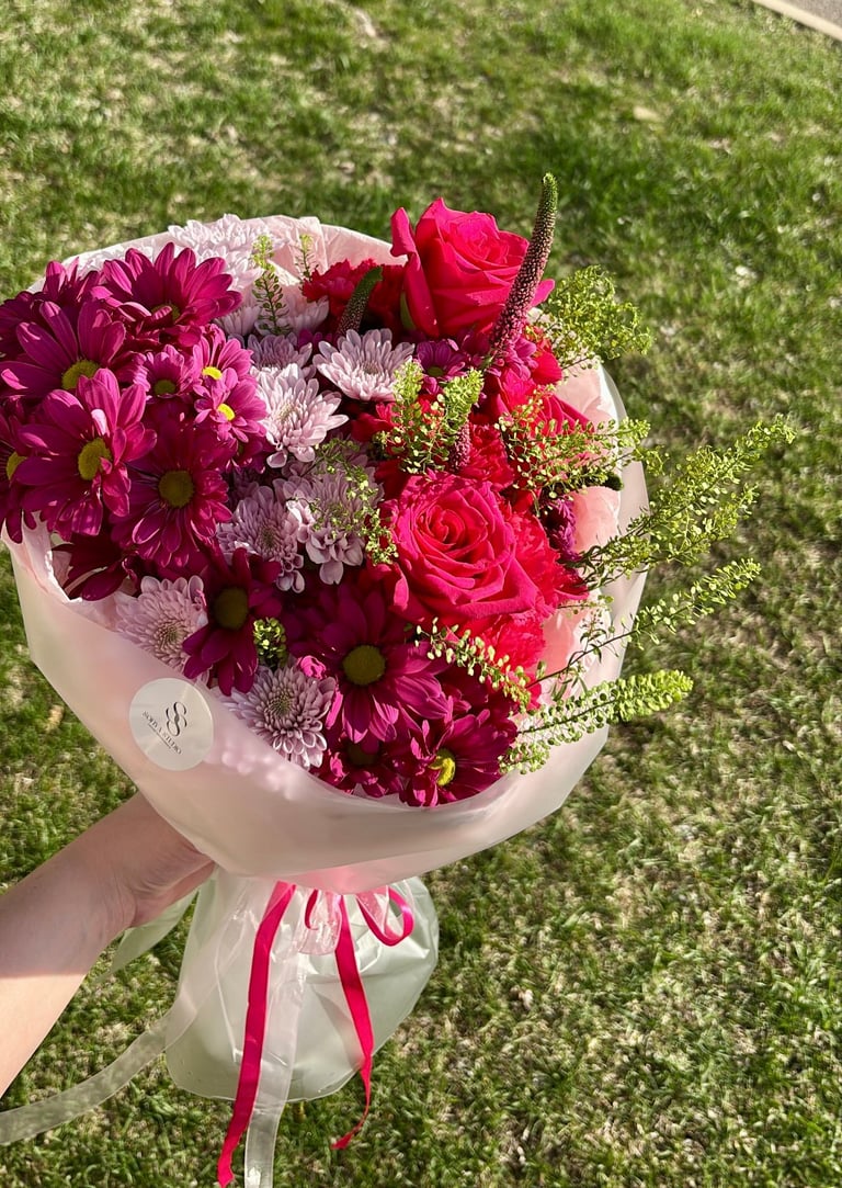 Red roses, pink flowers, and greenery in white paper with pink ribbon