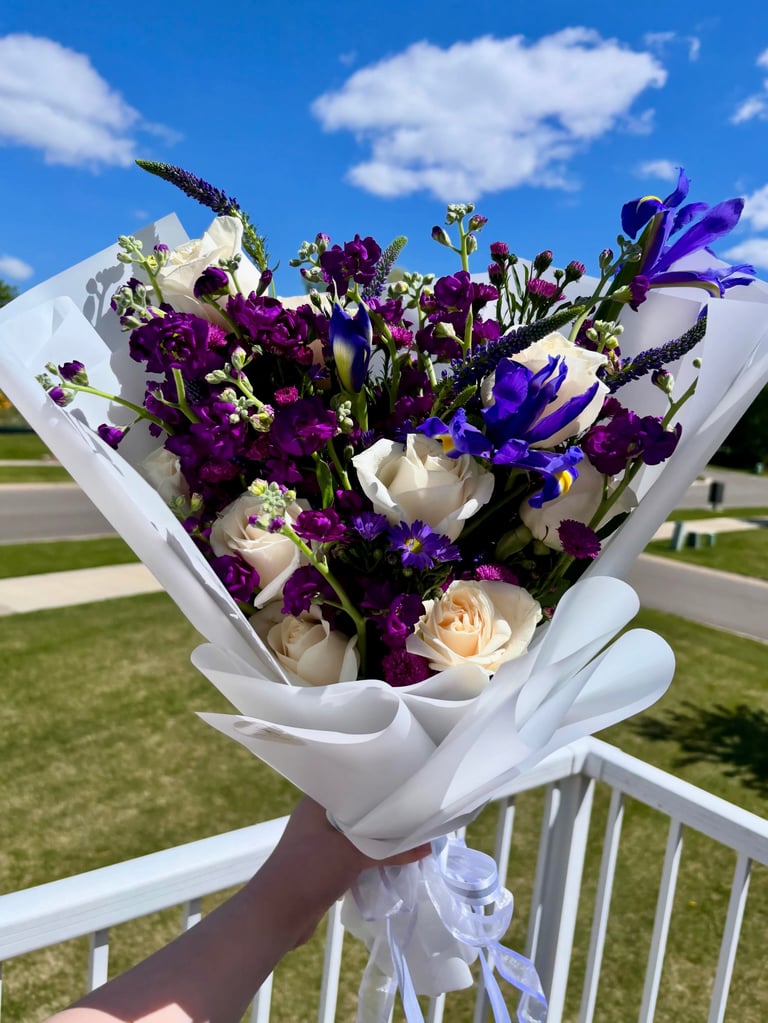 Purple irises, dark purple carnations, cream roses in white paper