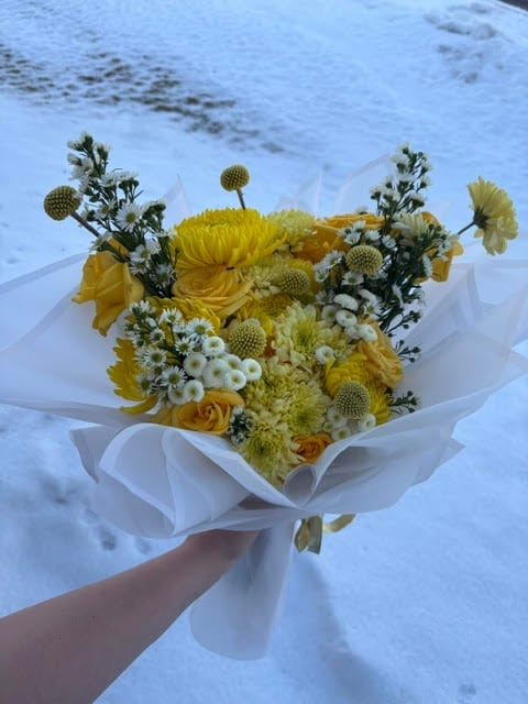 Hand holding a bouquet of yellow flowers with white wrapping on a snowy surface