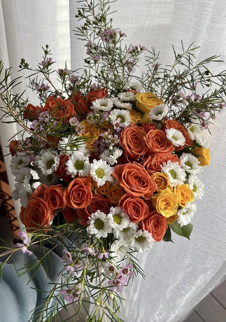 Colorful bouquet featuring orange and red roses with daisies and purple accents